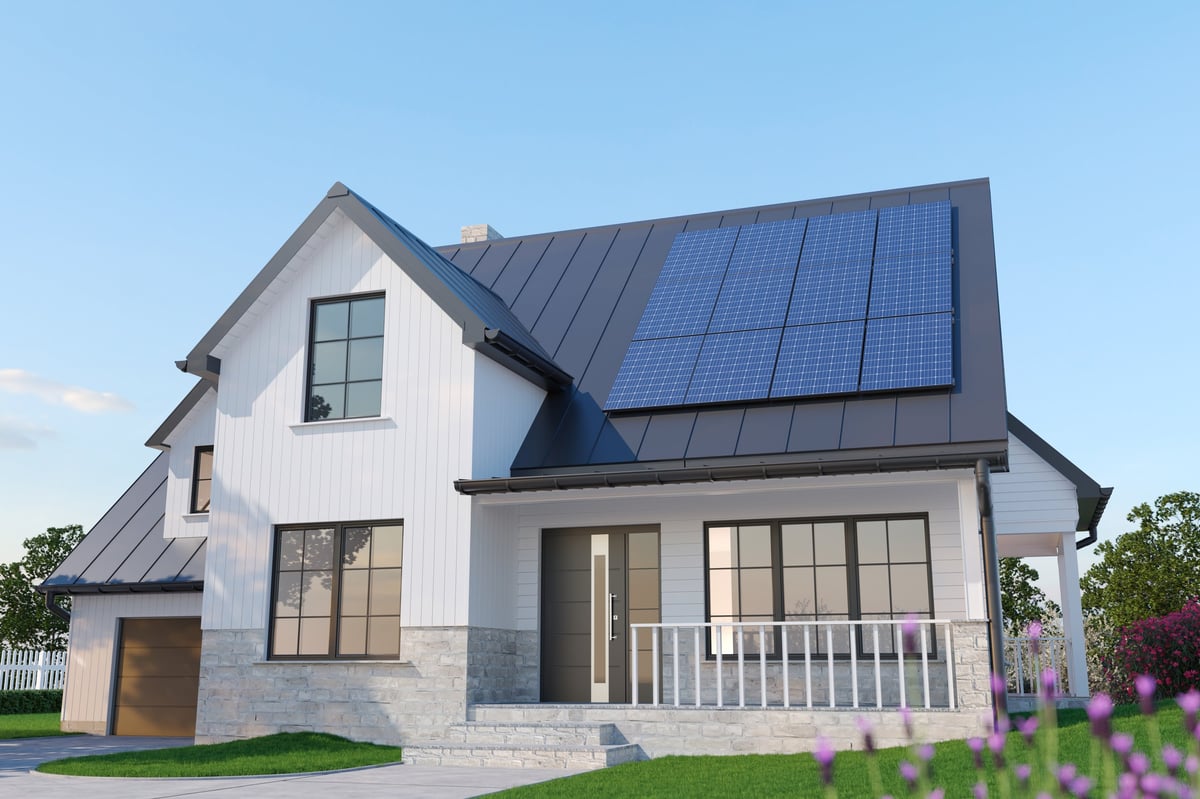 Modern single-family American house with rooftop solar panels installed on a dark metal roof. Sustainable suburban home architecture showcasing renewable energy, clean electricity generation and eco-friendly living concept. Contemporary residential exterior under clear blue sky.